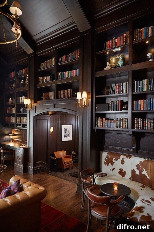 A cozy wood-paneled library with leather seating and shelves above doorway heights.