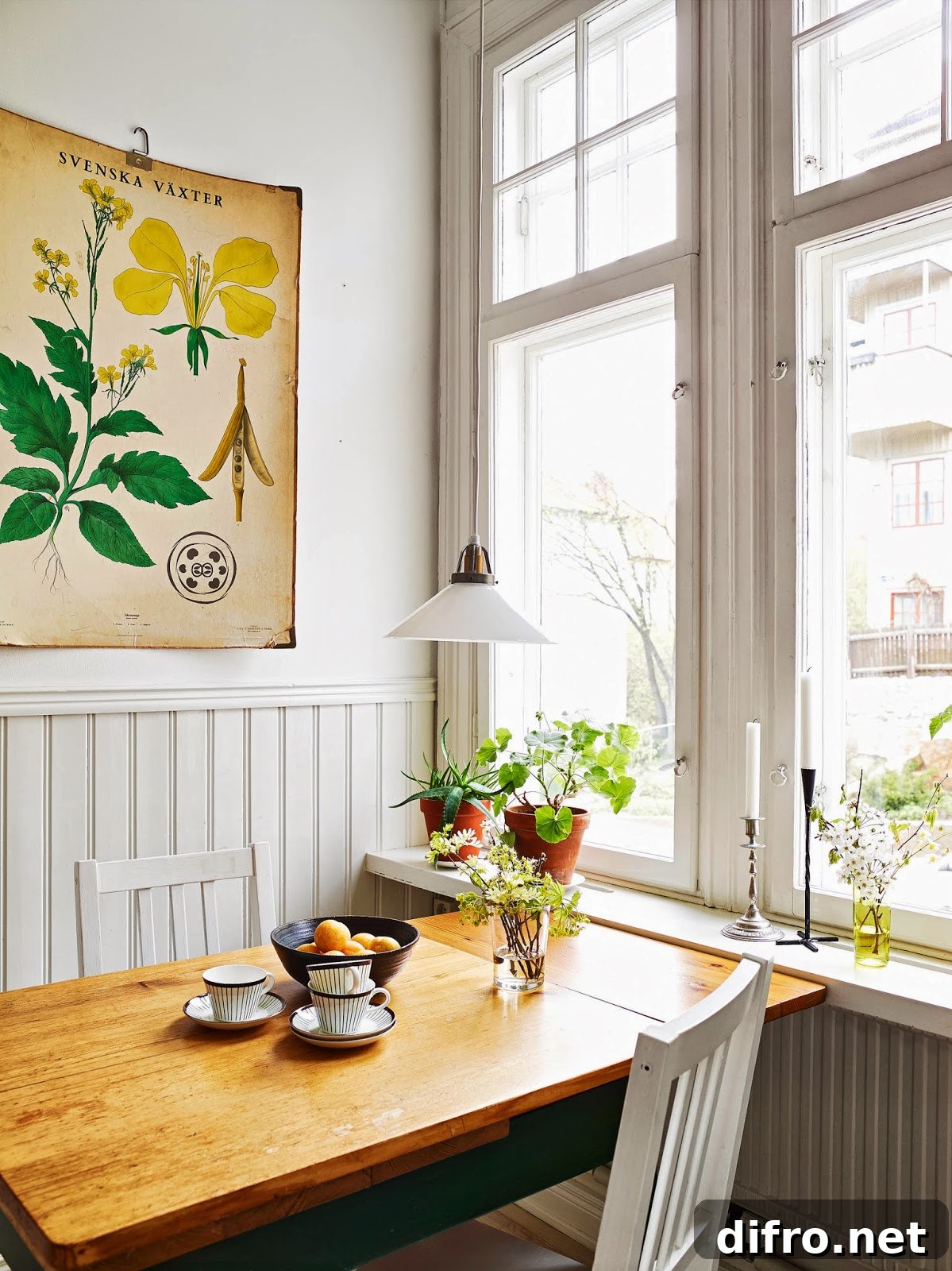 A wooden table with two chairs arranged around it sits in front of a large window. The table is set with a vase of flowers.