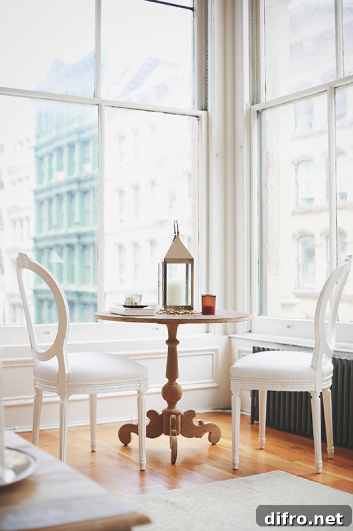 A room with large windows features a wooden table and chairs. The chairs have soft cushions and are positioned to enjoy the view outside.
