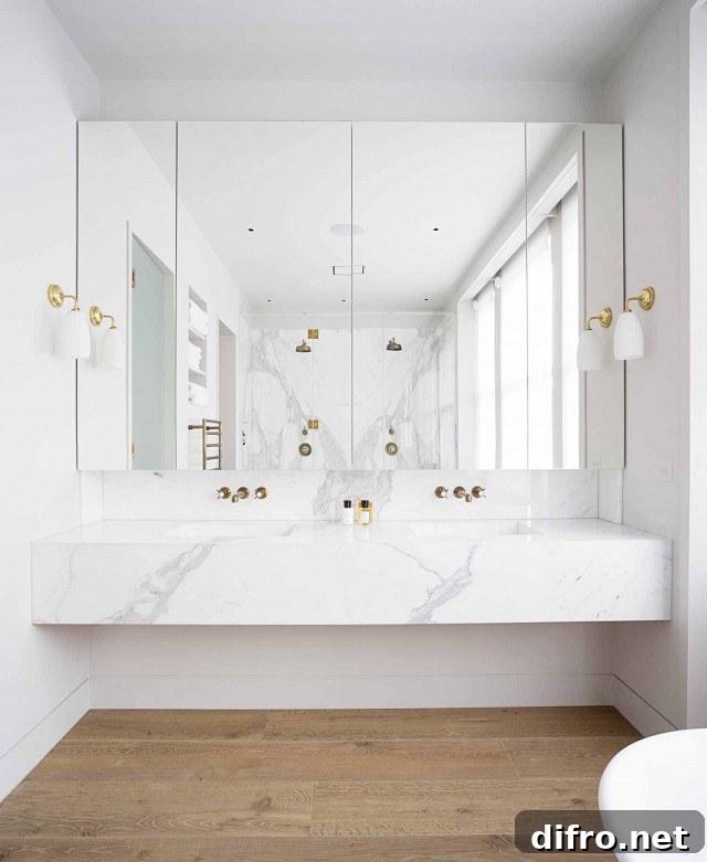 Modern bathroom features a floating marble vanity fitted with his and her sinks and gold faucets under mirrored medicine cabinets illuminated by white glass and gold sconces.
