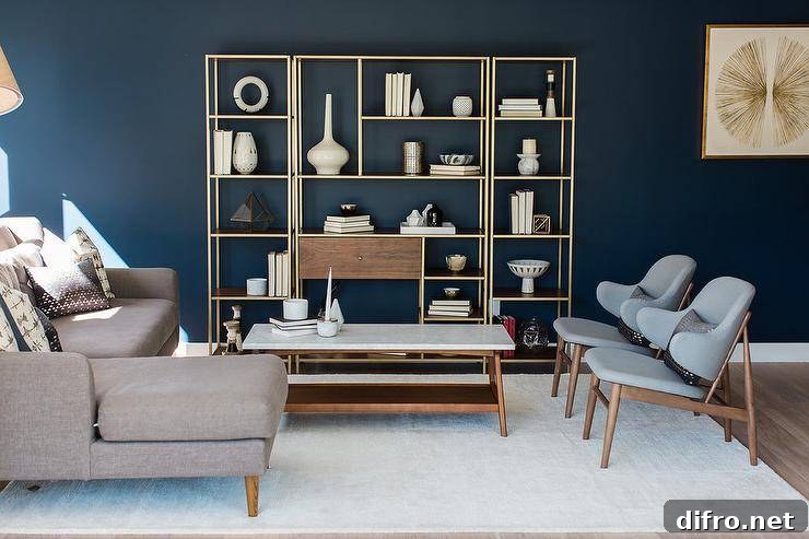Blue mid-century modern living room features deep blue walls positioned behind a wood and brass 3 piece styled shelving unit that faces a marble top mid-century modern coffee table flanked by a taupe sofa with a chaise lounge and two side by side blue mid-century modern chairs placed on a white wool rug.