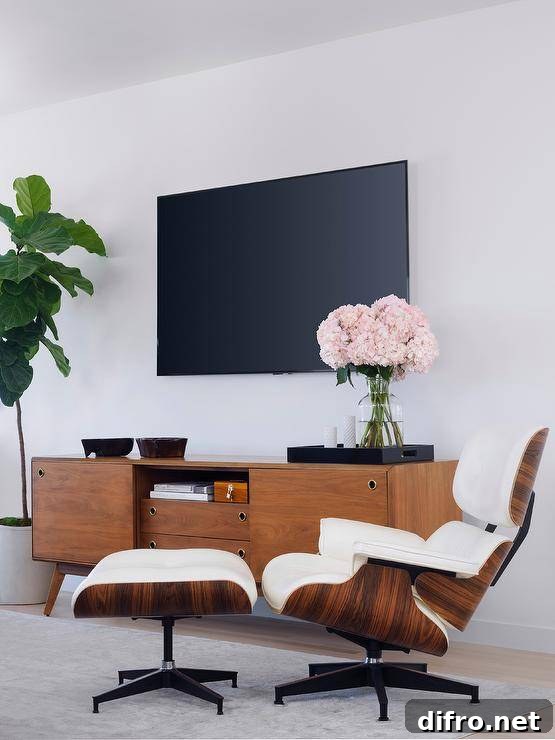 An Eames Lounger & Ottoman sits on a light gray rug in front of a mid-century modern TV console placed beside a fiddle leaf fig plant and under a flat panel TV.