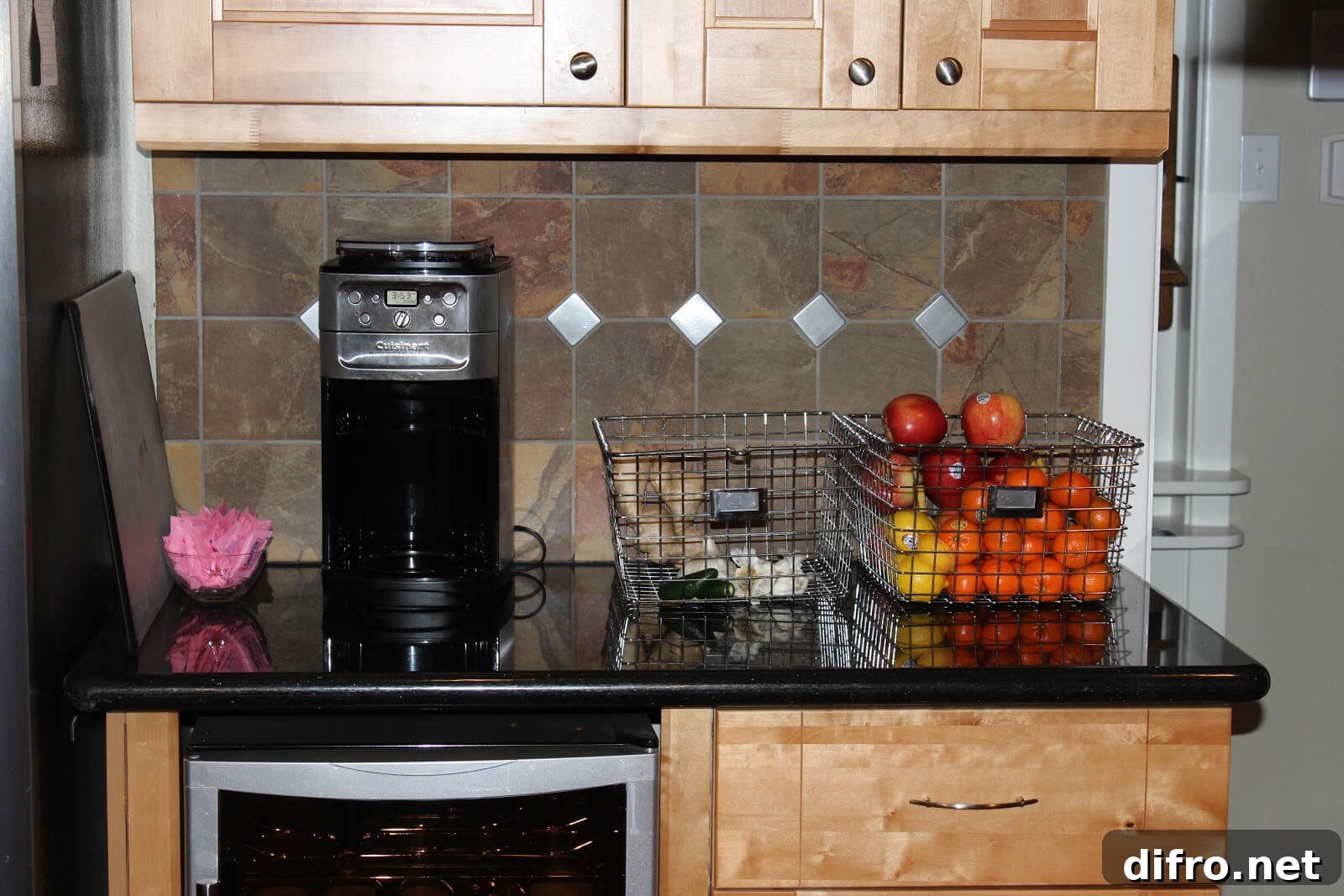 black kitchen countertop with light wood cabinets wire baskets on counter with fruits coffee maker