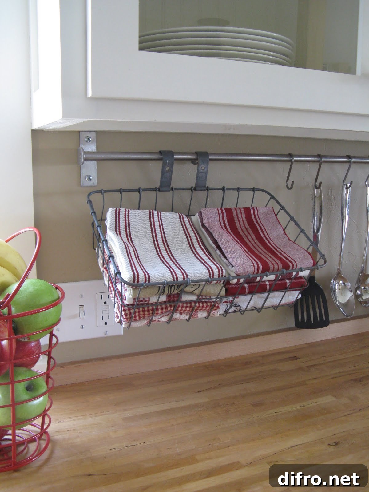 upcycled bicycle basket being used under kitchen cupboard with red dish towels inside