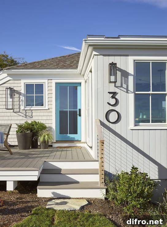 Cottage home features a turquoise blue front door with glass panels and gray siding completed with modern black house numbers.