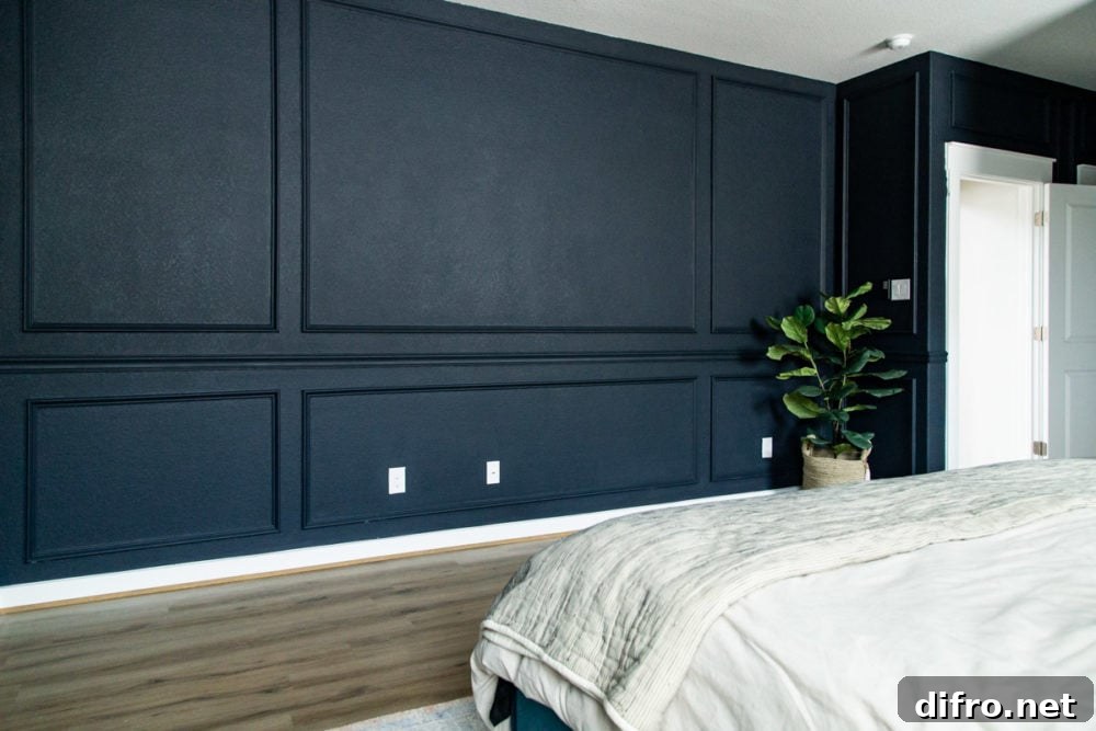 Dark-painted bedroom wall with moldings, green plant, white bed and white doorway