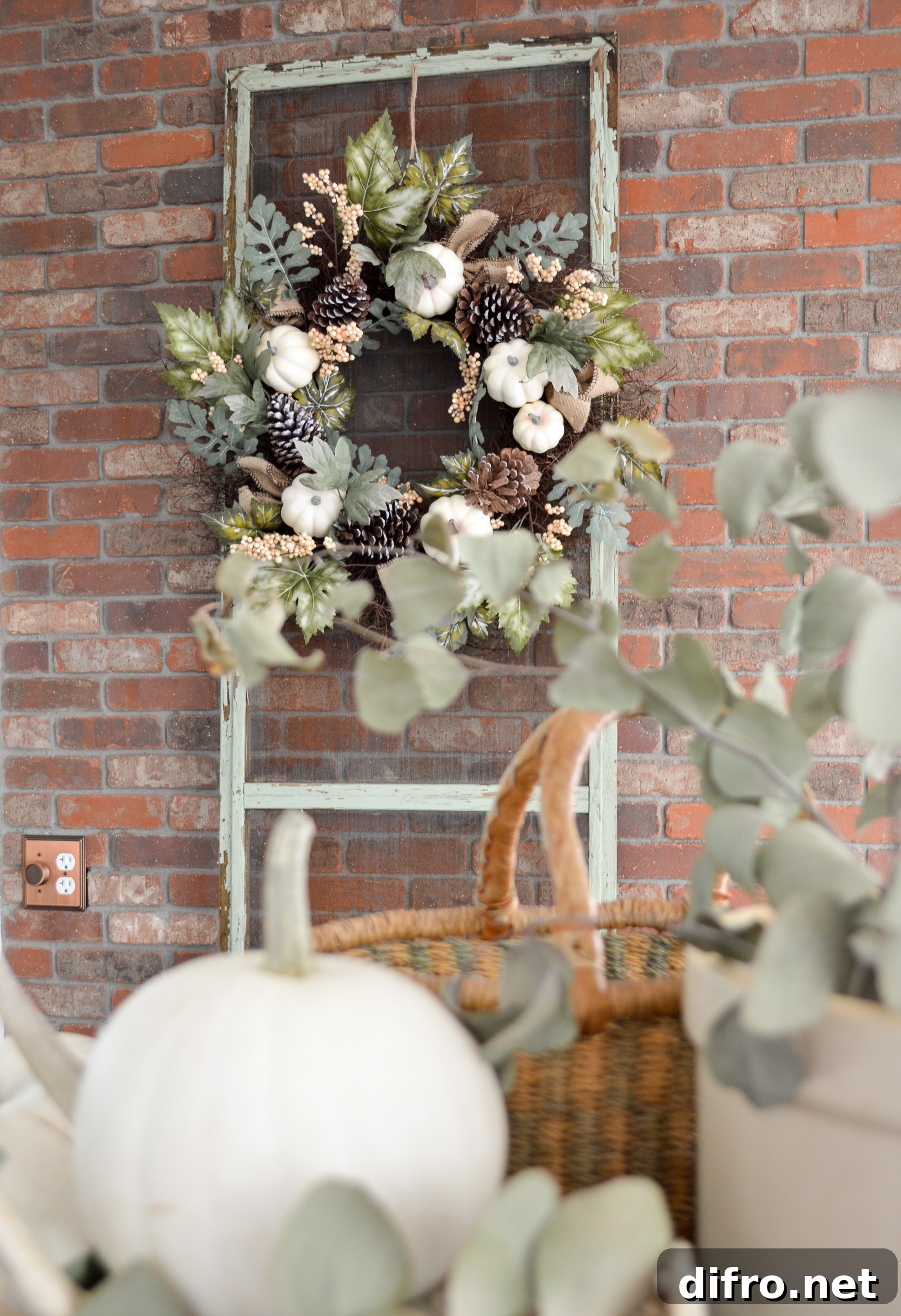 fall wreath hanging on old screen window up against red brick with pumpkin in foreground