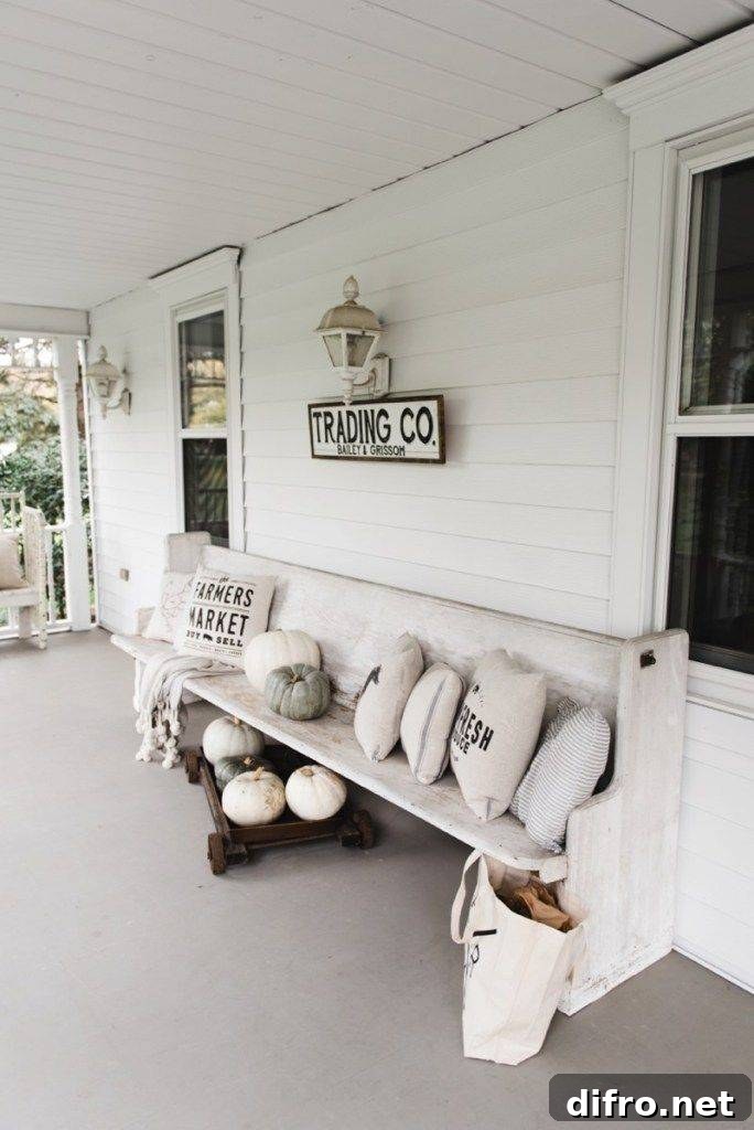 white porch pew with pillows and pumpkins along white sided house