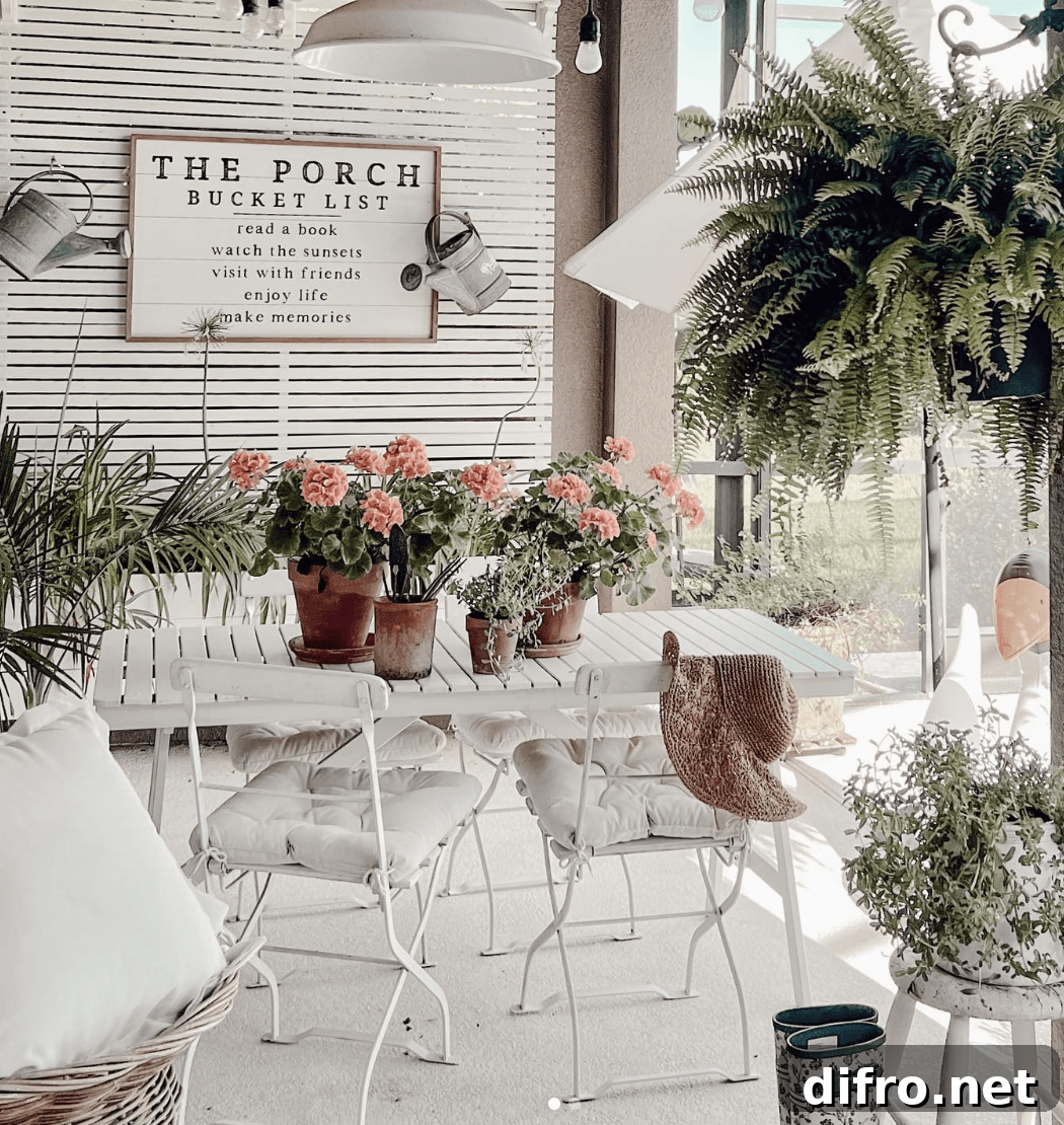 white patio furniture on porch with farmhouse style sign on wood slat wall fern potted plants on table pillows