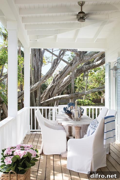 Whitewashed French oval dining table with white slipcovered chairs designed in an outdoor porch in a cottage home