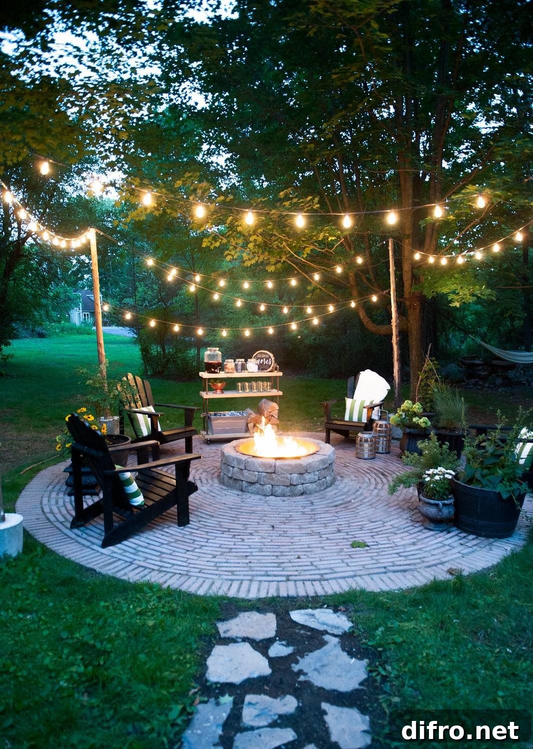 Outdoor fire put surrounded by black chairs, plants and dangling lights