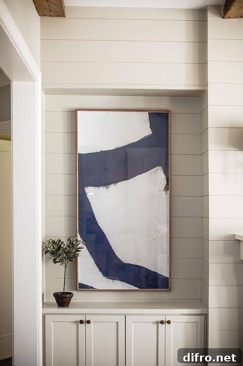 Living room features blue abstract art over light gray fireplace built-in shiplap wall cabinet with light gray shiplap trim.