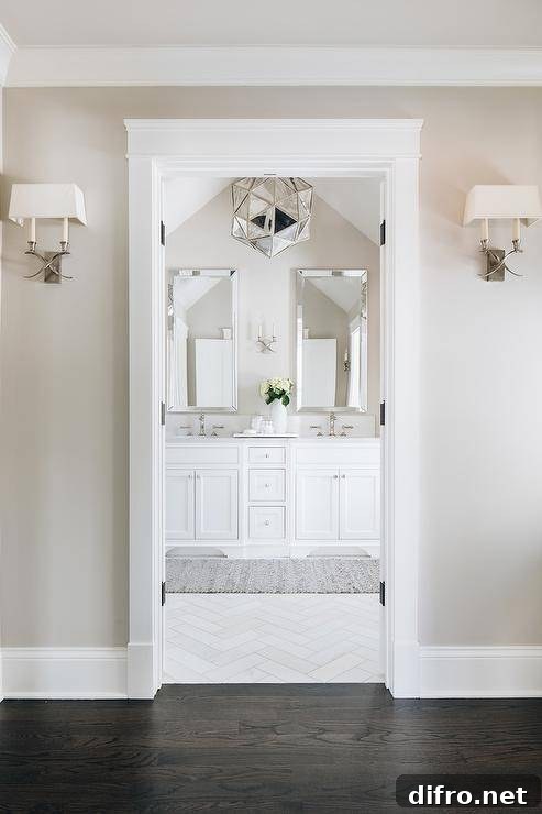 Beautiful master bathroom boasting white and taupe color tones accented with elegant finishings and stylish fixtures. A mercury glass chandelier brings a unique and luxurious appeal with a geometric touch in a spa-like bathroom design.