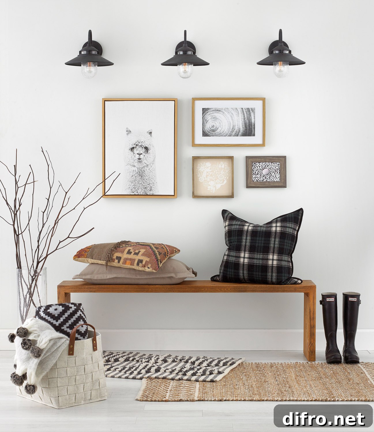 A bench with a pillow in an entryway with shoes beside it and framed pictures on the wall.
