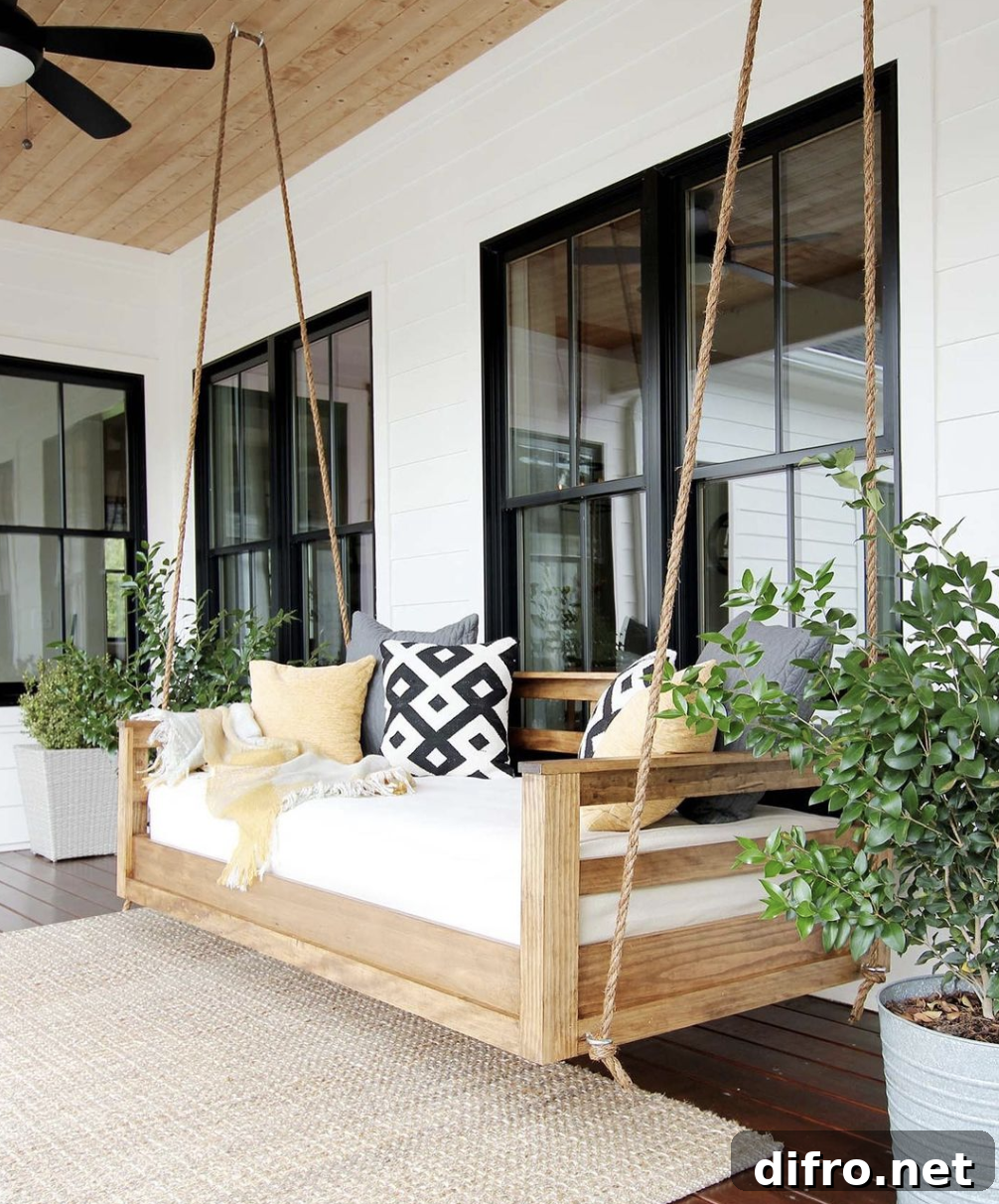 wood frame hanging patio porch bench swing with cushion black and yellow decor pillows black frame windows white siding house