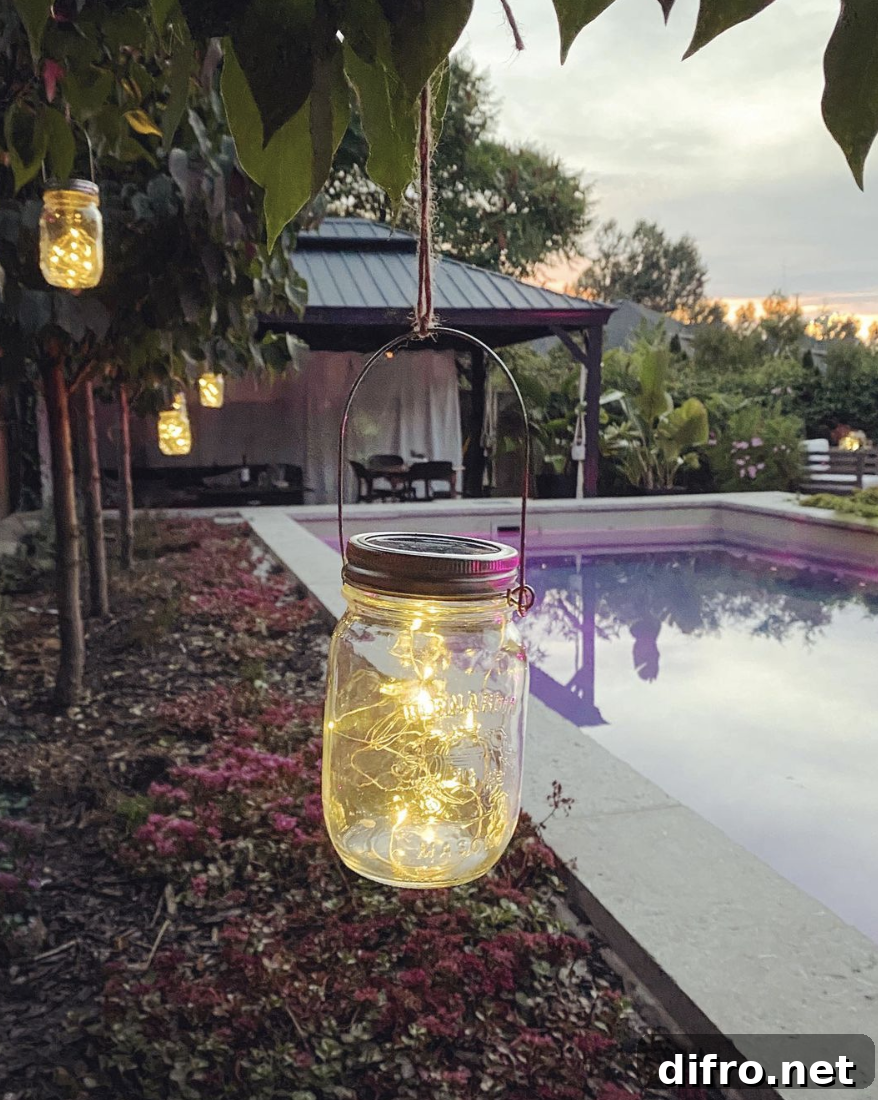 mason jar with string lights inside hanging from tree by pool