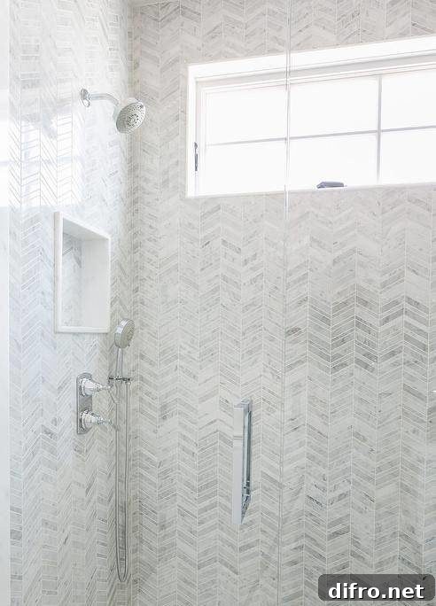 Walk in shower features gray marble chevron tiles and a tiled shower niche