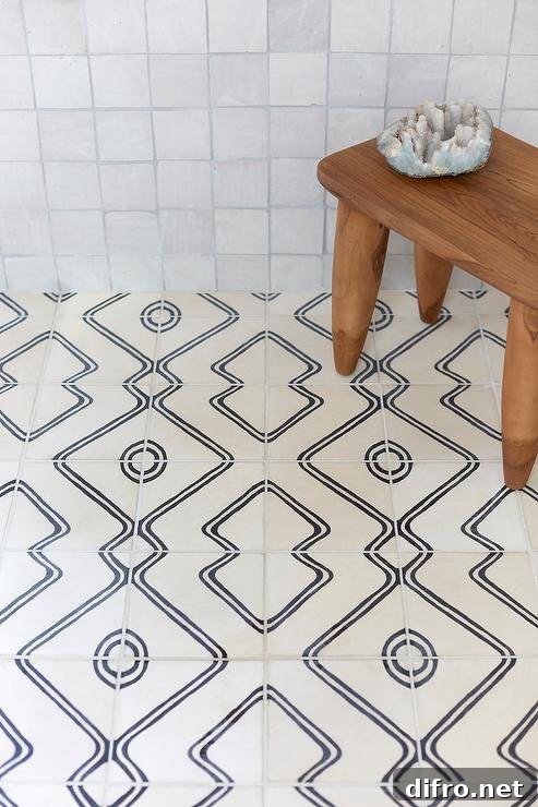 A teak stool sits in an expansive walk-in shower on ivory and black floor tiles and in front of gray glazed grid tiled walls