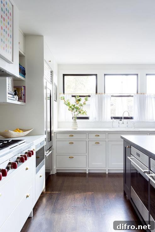 Vintage brass cup pulls on white inset cabinets in a transitional kitchen boasting honed white marble countertops and cafe curtains on a brass rod