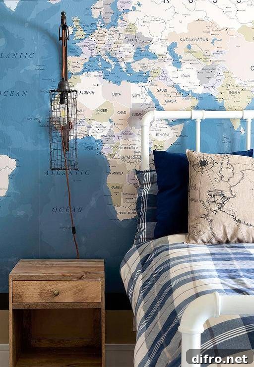 A cage sconce hangs from a wall covered in a world map mural over a reclaimed wood nightstand placed beside a vintage white metal pipe bed dressed in blue plaid bedding.