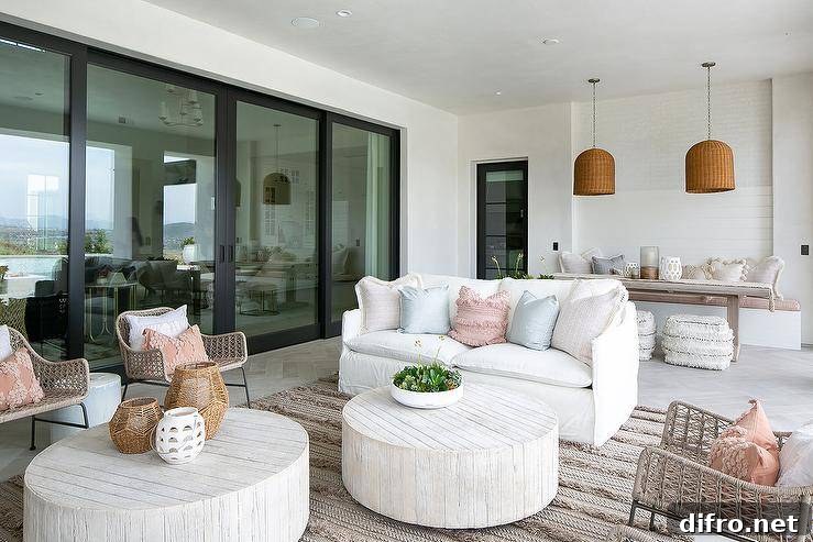 White slipcovered sofa with blue and pink pillows facing two round faux bois coffee tables under a covered patio.