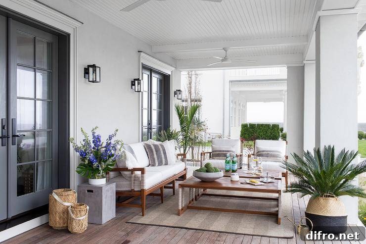 Outdoor covered patio designed with a brown bound herringbone sisal rug and a teak outdoor sofa with white cushions.