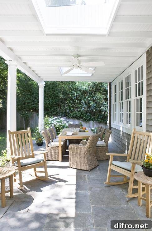 Covered patio features teak rocking chairs on slate pavers with round side tables.