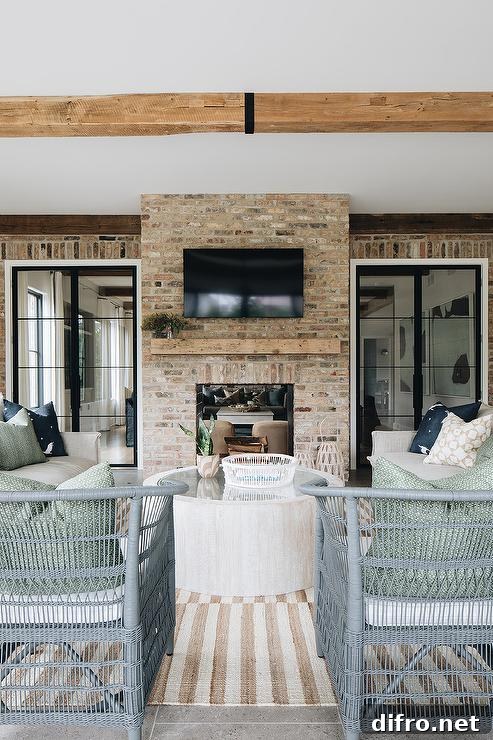 Covered patio with a TV above a rustic mantel, chairs on a striped rug facing the fireplace.