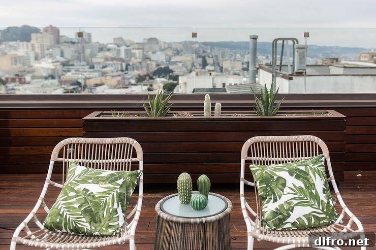 Two rope outdoor chairs with palm leaf pillows on an outdoor dark stained oak patio with a city view. A reeded outdoor accent table is styled between the two chairs displaying succulent decor.