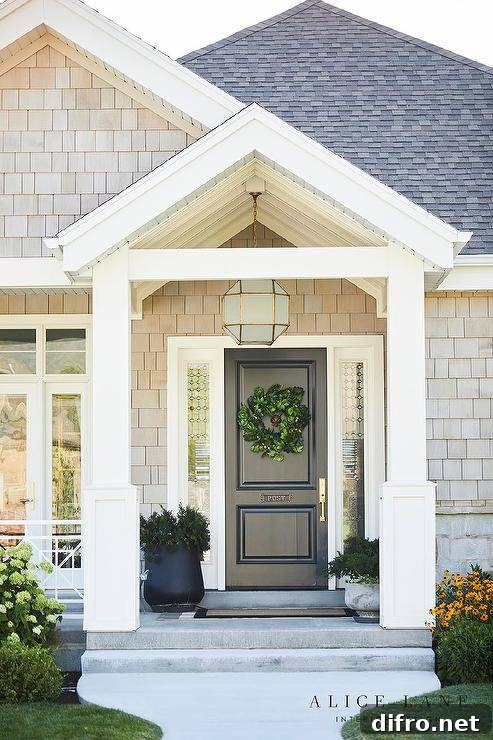 Suzanne Kasler Morris Lantern fitted above a black front door in a covered porch with a black border doormat and styled potted plants.