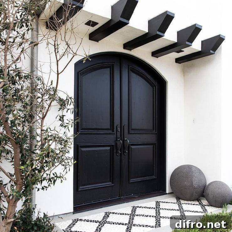 Mediterranean style home with white stucco features black double front doors with stylish black and white porch tiles and gray cement boulder accents.