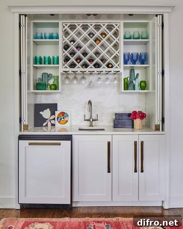 Folding doors conceal a wet bar nook boasting white shaker cabinets accented with long brass hardware and a honed marble countertop holding a small sink under a brushed nickel faucet.