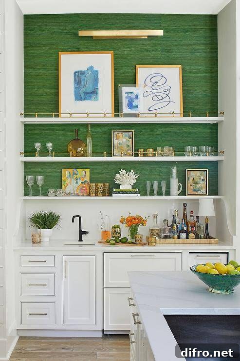 A brass picture light fixed to an emerald green grasscloth wall lights styled and stacked white and gold shelves above white bar cabinets.