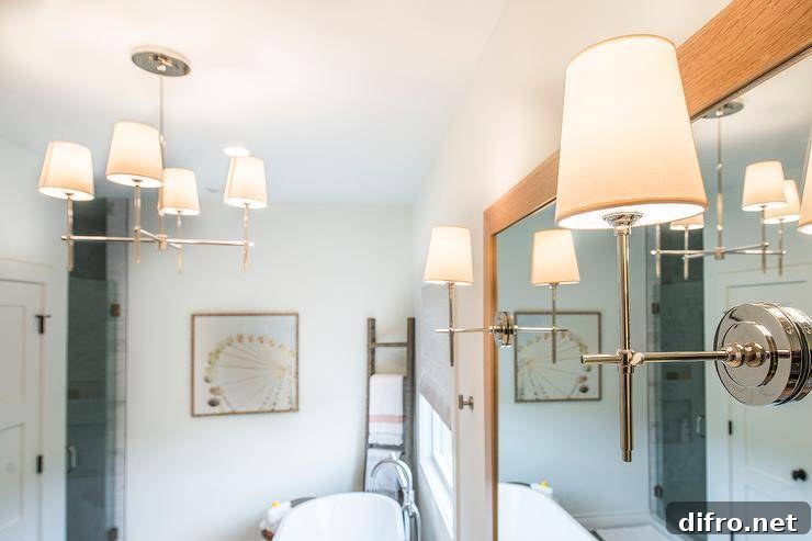 Master bathroom with shaded mirror and pendant lighting from Circa Lighting, a freestanding white tub, and a natural wood mirror over a custom vanity. Natural wood, blush, and navy all accent the white color scheme of the space.