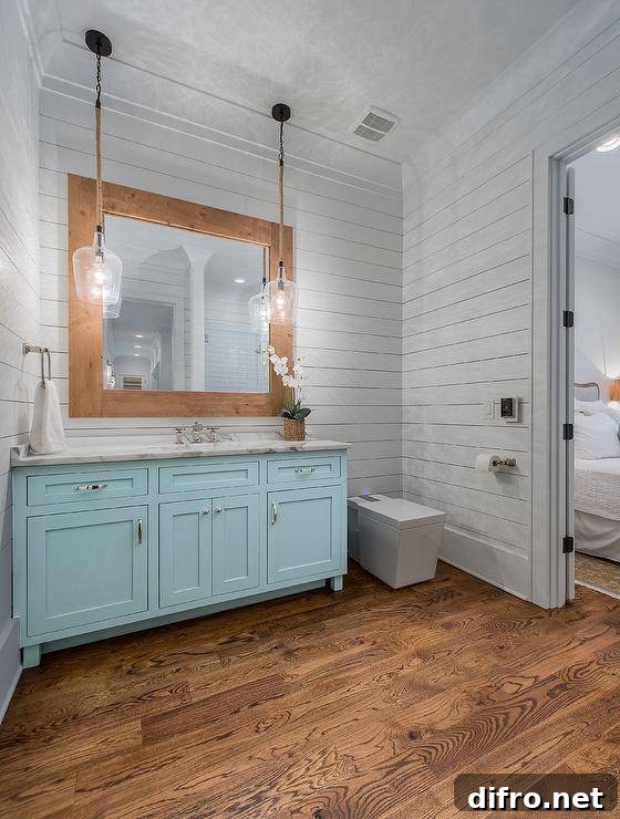 Rustic glass and rope lights over a turquoise blue bath vanity with a white marble top. White shiplap walls offer a cottage feel surrounding stained oak hardwood floors complimenting a wood framed vanity mirror.