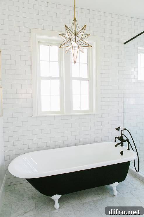 Black and white bathroom features walls lined with white subway tiles alongside a brass and glass star pendant, Pottery Barn Glass Star Pendant, illuminating a black claw foot tub paired with an oil rubbed bronze tub filler next to a seamless glass shower.