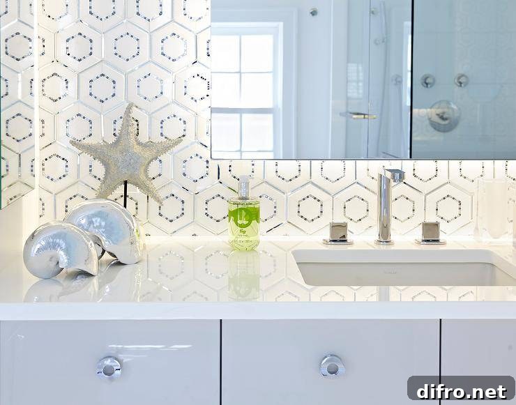 Contemporary bathroom features a frameless vanity mirror fitted with custom behind mirror lighting that's illuminating white and silver hex backsplash tiles and a white quartz countertops holding an undermount sink and polished nickel modern faucet positioned over flat front lacquered gray vanity cabinets finished with round polished nickel modern pulls. The room is completed with decorative silver seashells and silver starfish on a black stand.