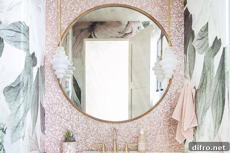 A round gold mirror hangs from pink iridescent backsplash tiles lit by brass and rippled glass mini pendants fixed over a brass faucet kit.