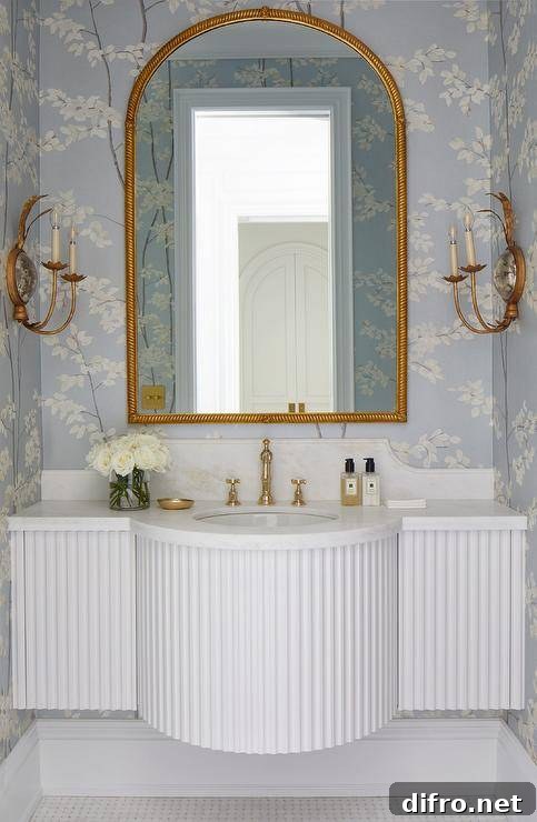 gold arch mirror in half bathroom with white pole wrap sink gold candle wall sconces with floral wallpaper