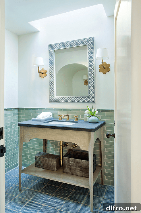 Chic powder room features a skylight illuminating a white and black bone inlay mirror flanked by scalloped brass wall sconces, Hudson Valley Lighting Pomona Sconces, as well as a beige washstand topped with honed black marble.