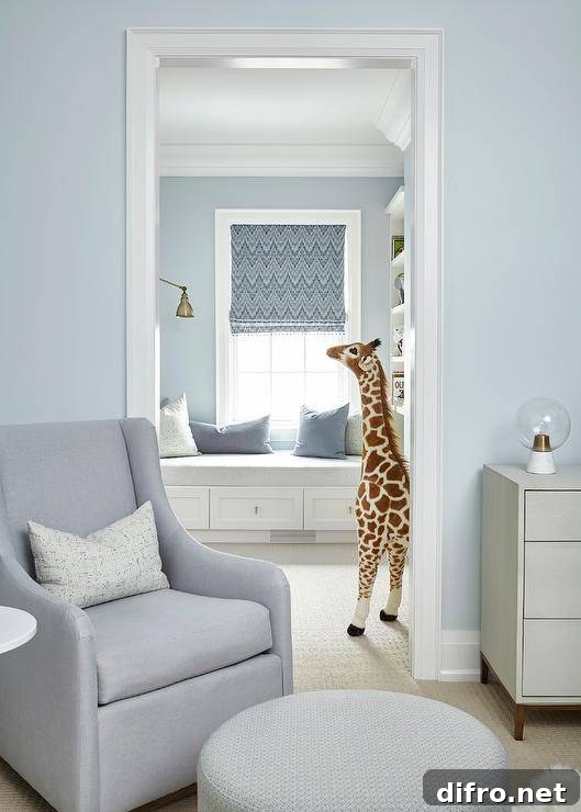Gray nursery glider with a round ottoman in a nursery room painted in light blue with neutral furnishings.
