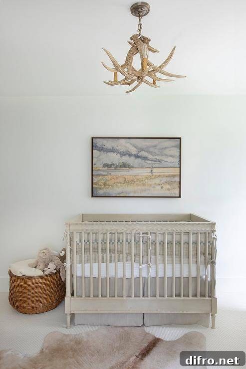 A tan cowhide rug sits on off-white carpet in front of a gray wooden crib accented with a gray crib skirt and placed beneath a framed landscape art piece. The room is illuminated by a faux antlers chandelier.