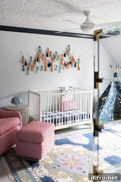 Eclectic red and blue boy's nursery features a white wooden crib placed beneath tassel art hung from a white wall lined with black crown moldings framing a white and gray wallpapered ceiling. The crib is flanked by a red rocker and ottoman and a yellow and blue teepee.