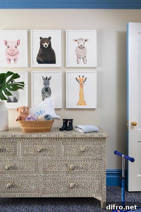 Bright blue crown moldings and baseboards accent an ivory painted wall holding a gallery of framed baby animal sketches over a cream and black bone inlay dresser in a wonderfully styled nursery.
