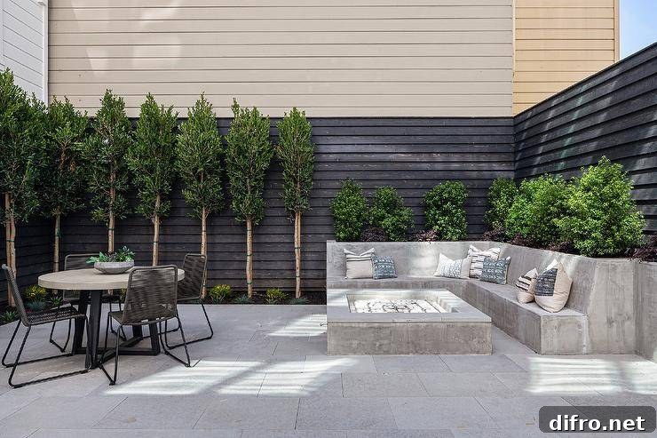 A built-in l-shaped concrete sofa sits in a backyard at a concrete firepit, with gray rope chairs around a concrete and metal dining table.
