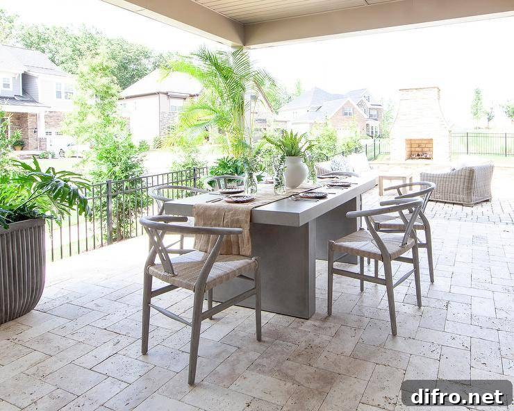 Wishbone chairs surround a concrete dining table on a covered patio with cream pavers.