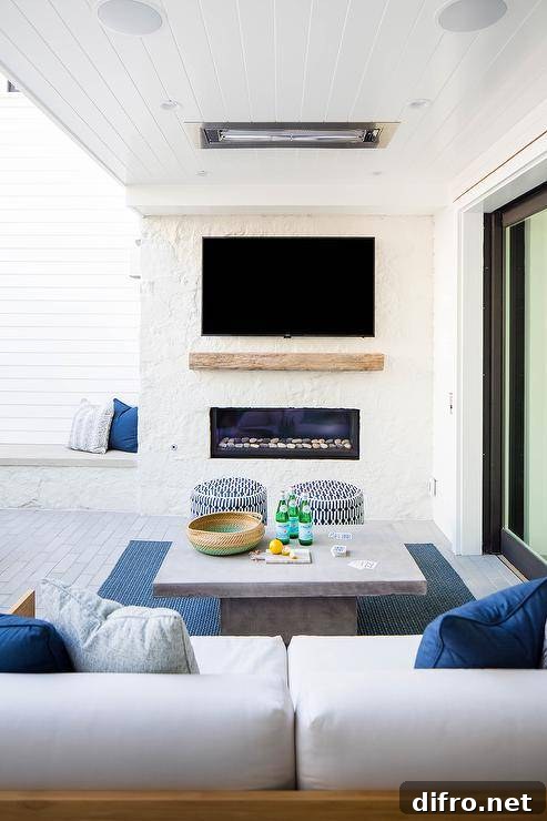 A covered patio with teak sofas and a concrete coffee table, featuring a wall-mounted TV and fireplace for outdoor entertainment.