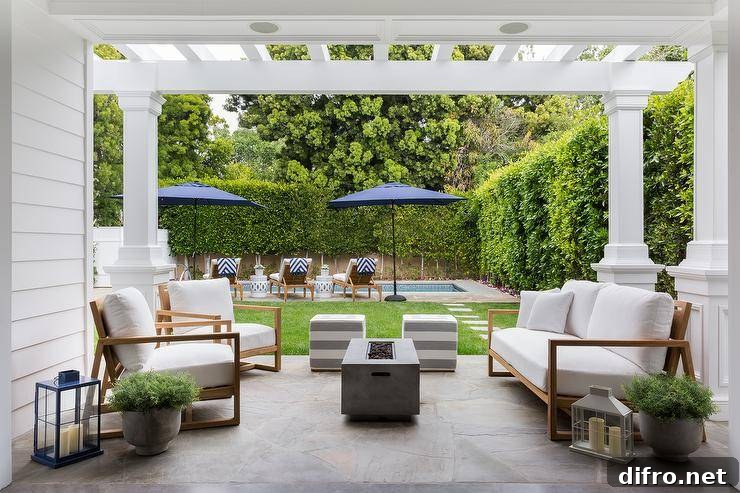 Under a pergola, a rectangular concrete fire pit sits between teak seating.