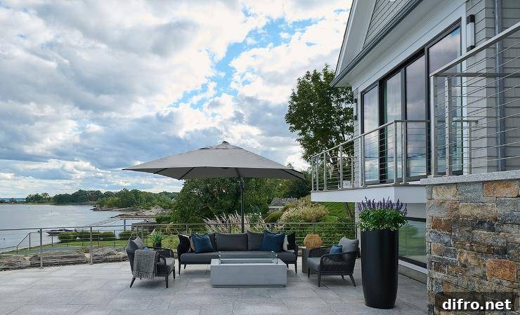 A concrete fire pit with black rope seating under a gray umbrella.