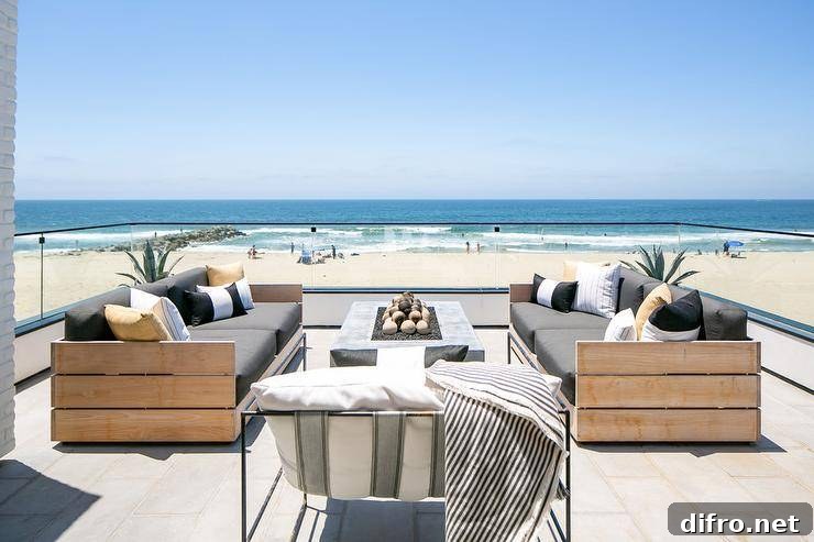 Beachfront outdoor patio features teak slatted outdoor sofas with a concrete fire pit on pavers finished with a glass enclosure.